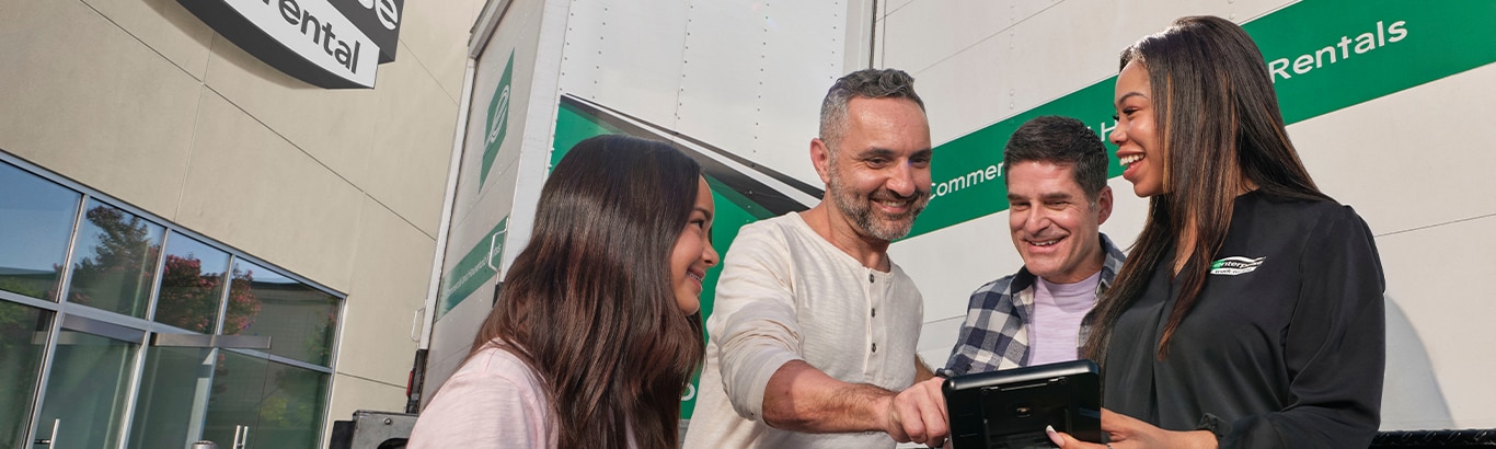 Woman holding a tray of flowers just unloaded from a pickup truck parked in her driveway while looking at a man holding a shovel in the front yard