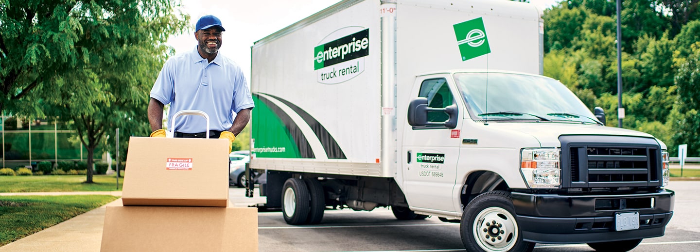 Hombre empujando cajas en una carretilla de mano frente a una van de transporte de Enterprise